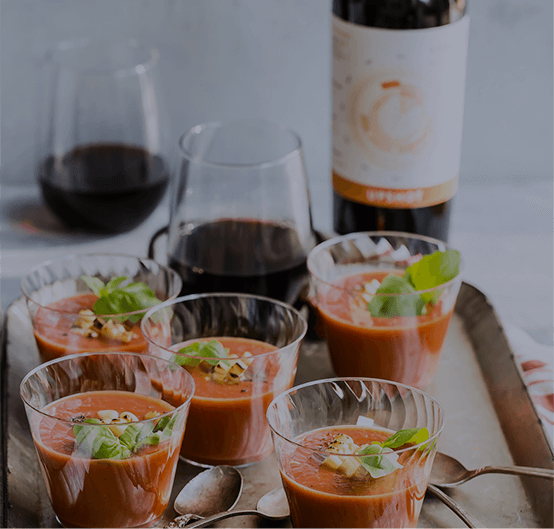 Closeup of small cups of Roasted Veggie Tomato Gazpacho and glasses or red wine on a tray
